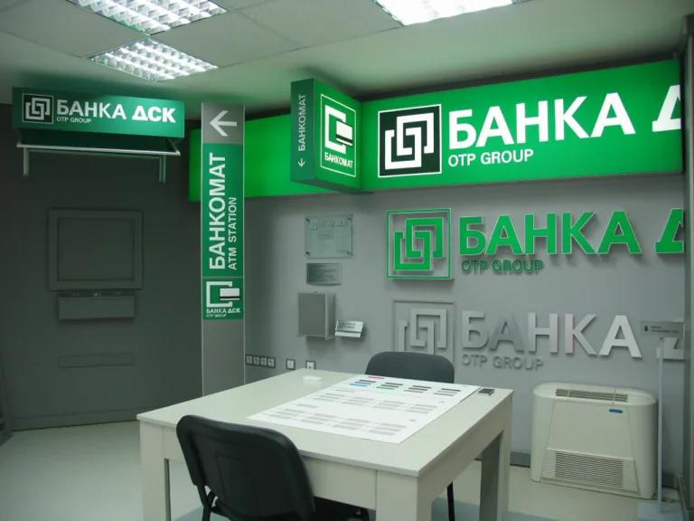 Интериор на банков офис с брандирани светещи табели, указателни елементи и обемни лога на Банка ДСК по стените.