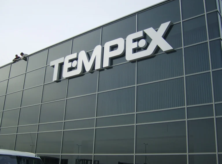 Големи обемни букви с надпис TEMPEX, монтирани върху стъклена фасада на модерна офис сграда.