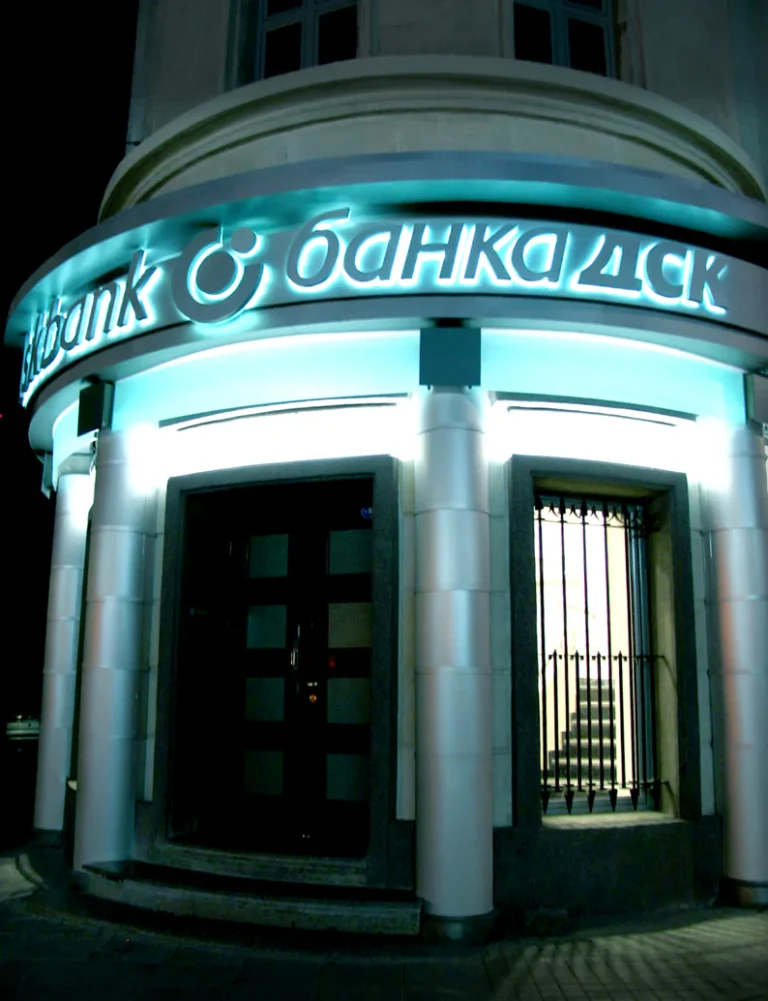 Светещи обемни букви с логото на Банка ДСК, монтирани върху фасадата на сграда през нощта.