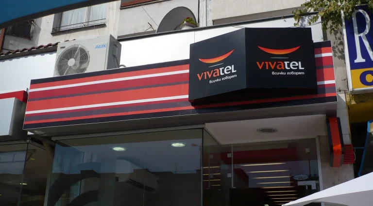 Външна реклама на търговски обект с брандирана табела и логото на Vivatel върху черна основа с хоризонтални червени и бели линии.